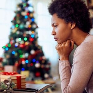 sad woman next to lit up Christmas Tree, coping with grief during the holidays.